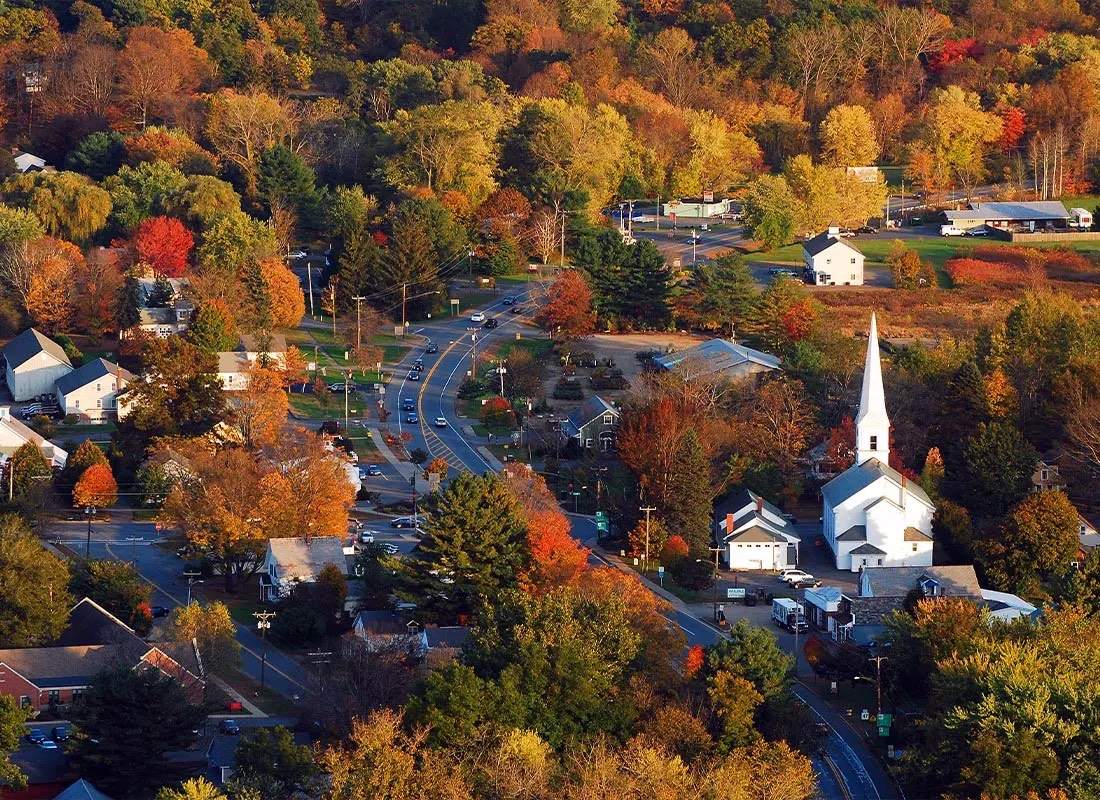 Aerial view of a South Windsor road winding past a white steepled church and houses in full autumn color